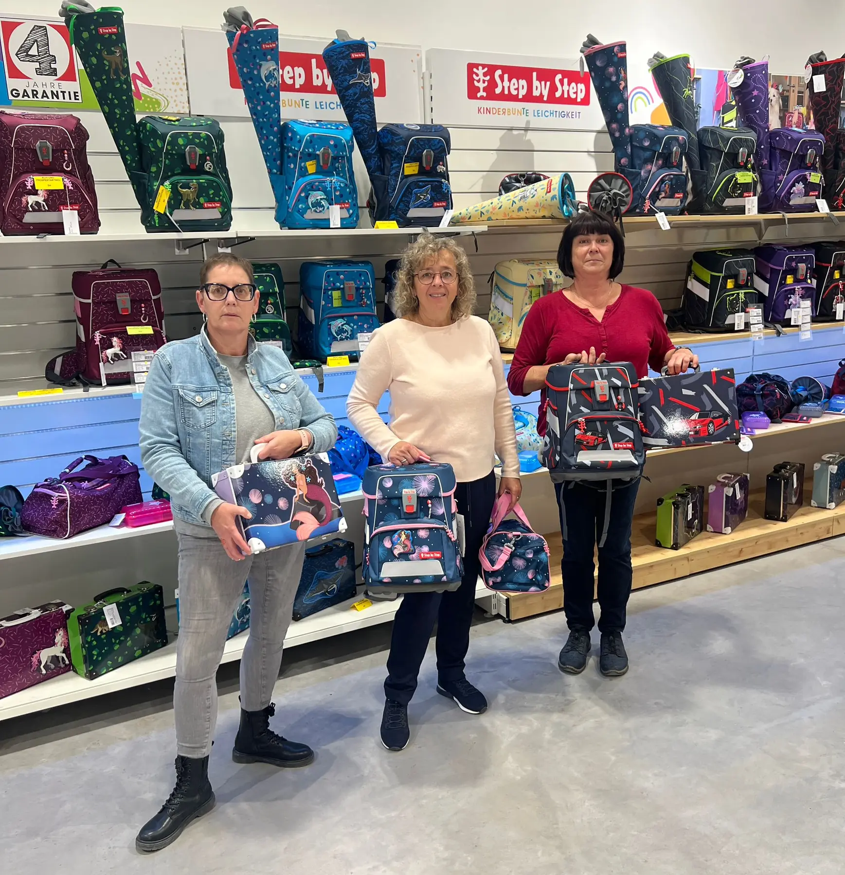 Drei Mitarbeiterinnen präsentieren Schultaschen im Geschäft